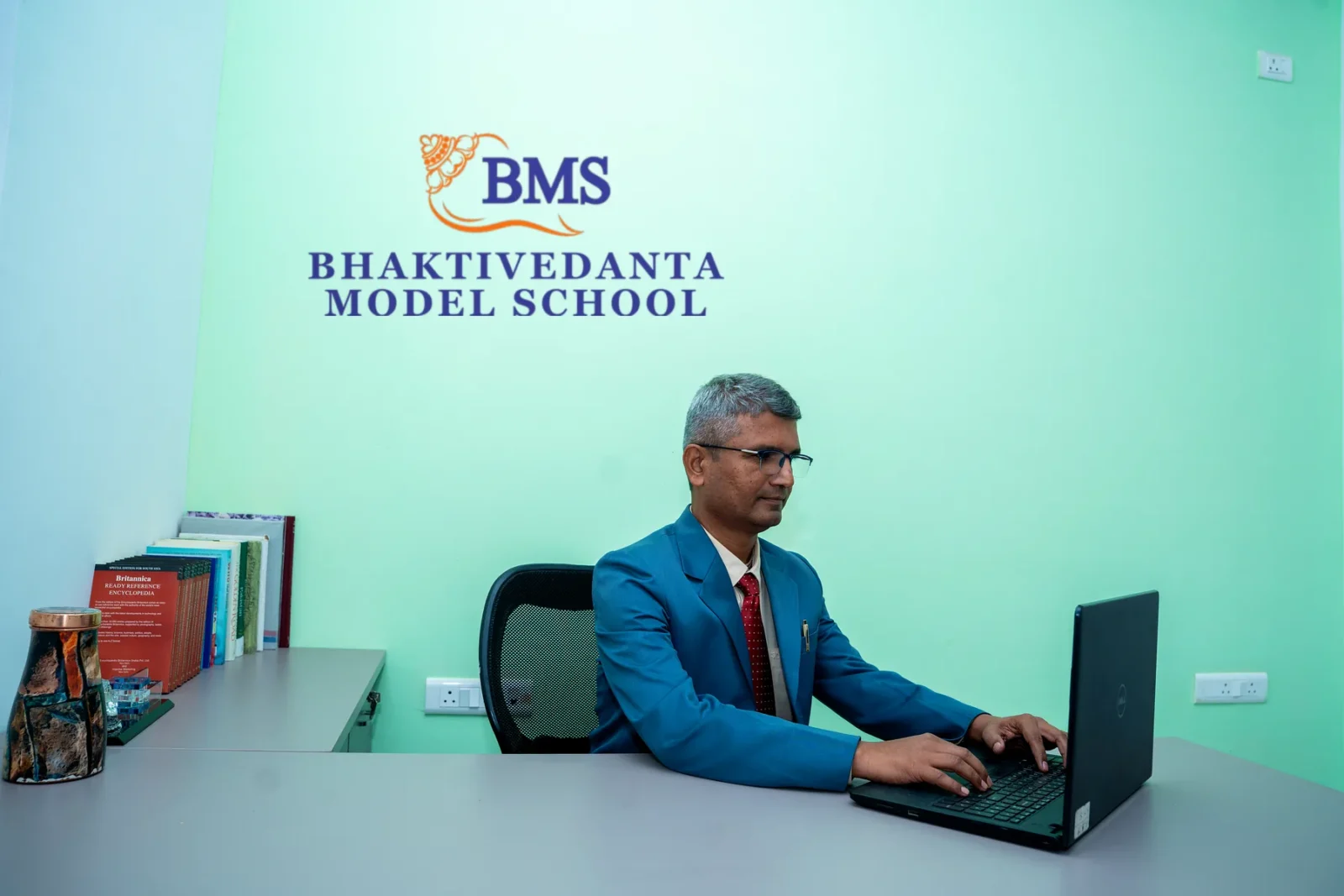 The Chairman at work in the Chairman's office, the school's crest and name on the wall behind him