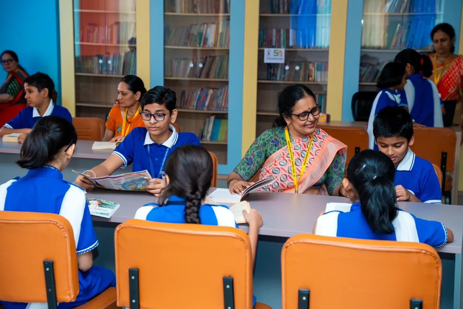 A teacher reading with a small group of children around the library tables